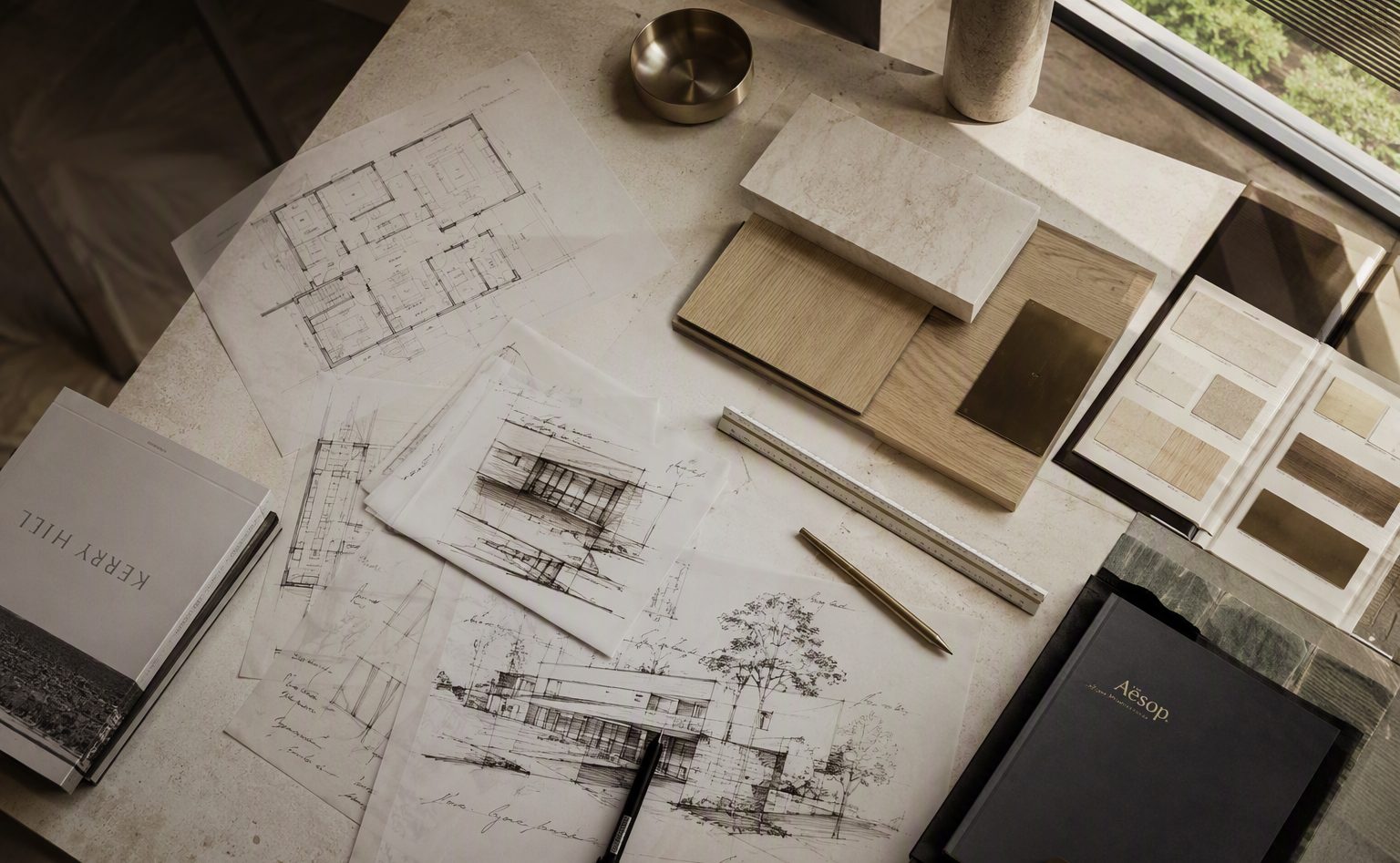 Design studio worktable with drawings, material samples of stone, oak and bronze